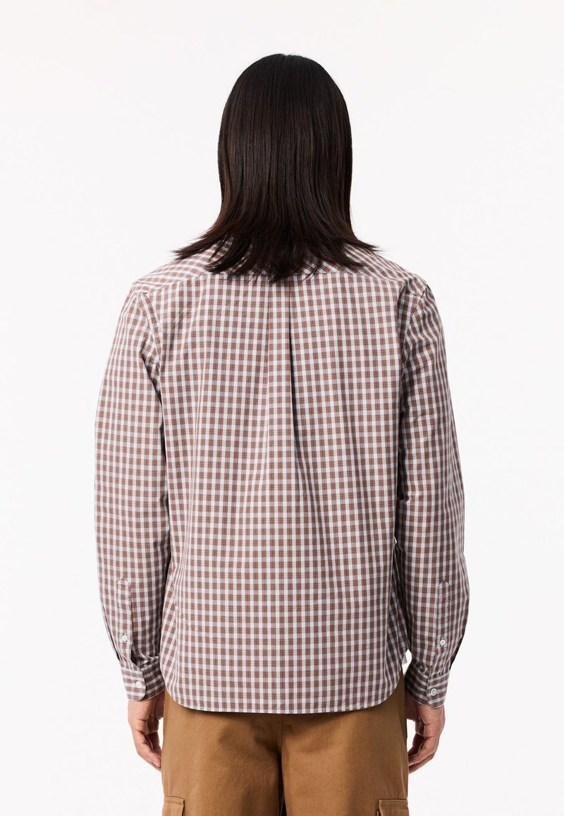 Chemise à manches longues à carreaux marron et blancs avec un col boutonné et un pli au dos, fabriquée à partir d'un tissu léger.