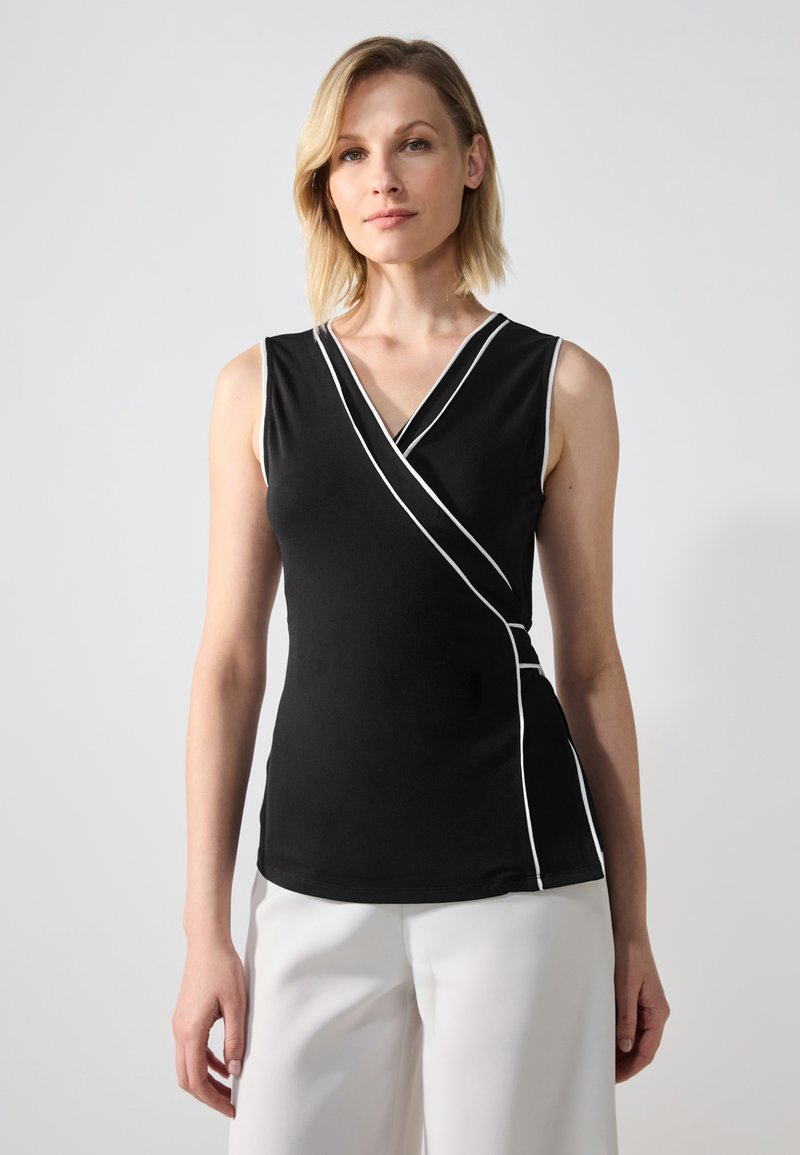 Musthave musta ilmaõlgadega topp V-kaelusega ja valge äärise detailiga, millel on mähisdisain ja sile tekstuur. Kombineeritud valgete pükstega.