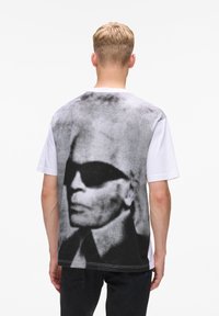 Weißes T-Shirt mit einem großen schwarz-weißen Grafikdruck eines Gesichts mit Sonnenbrille auf der Rückseite. Aus Baumwolle, mit kurzen Ärmeln und Rundhalsausschnitt.