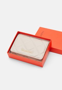 Išklota šviesiai ruda oda piniginė oranžinėje dežutėje; turi auksinę logotipą ir elegantišką stačiakampį siluetą su siuvinėjimo detalėmis.