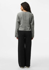 Chaqueta de mezclilla gris con mangas largas; cuenta con un escote redondo y longitud corta. Combinada con pantalones negros de pierna ancha.