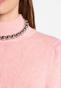Roze gebreide trui met een hoge kraag en geribbelde textuur, voorzien van een zilveren kraal ketting als opvallend detail.