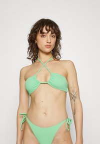 Zöld bikini szett, amely texturált felülettel, háromszög alakú melltartó résszel és keresztpántos kialakítással, valamint állítható megkötős alsó résszel rendelkezik.