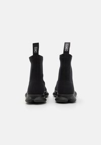 Botas de tobillo estilo calcetín en negro con parte superior de textil suave, suelas gruesas y lengüetas de tirón con el logo "Camper" en la parte posterior.