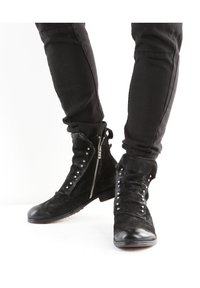 Bottes basses en daim noir avec des clous argentés décoratifs et des fermetures éclair latérales, dotées d'un embout arrondi et d'un petit talon empilé. Tissu texturé.