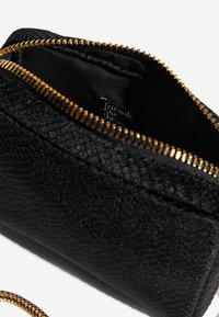 Borsa nera con texture e cerniera dorata. L'interno è foderato in tessuto nero, con un'etichetta che recita "friends like these".