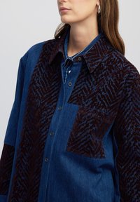 Denim overhemd met een donker bordeaux gekleurde textuurstof op de schouders en één zak, voorzien van een klassieke kraag en knoopsluiting.