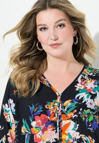 Blommig svart topp med v-ringning, färgglad blommig tryck, knappdetaljer och avslappnad passform. Mjuk tyg med en slät textur.