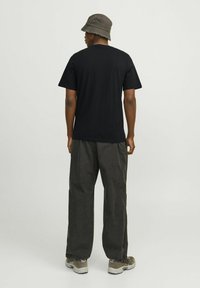 Zwart t-shirt met een ronde hals, gecombineerd met losse, donkergrijze broeken en een grijze bucket hat. Sneakers met lichte accenten.