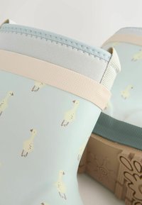 Hellblaue Gummistiefel mit einem Muster aus gelben Vögeln, ergänzt durch eine strukturierte beige Sohle und ein weiches elastisches Band am oberen Rand.
