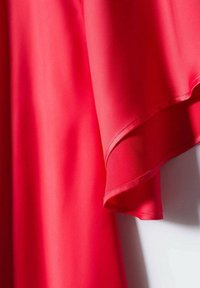 Tissu léger de couleur rouge vif avec une texture lisse. Le design présente des manches fluides avec un ourlet doux, accentuant une silhouette décontractée.