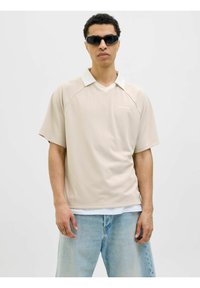 Beige, kortærmet polo skjorte med en hvid krave, der har et diskret lodret stribemønster og et logo på venstre bryst.