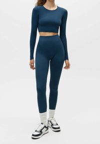Leggings taille haute bleu marine associés à un haut court à manches longues, présentant un tissu lisse et extensible avec des coutures minimales.
