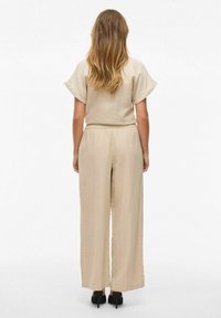 Ensemble en deux pièces beige avec des manches courtes et un pantalon à larges jambes. Tissu léger et texturé avec une taille élastique. Des talons noirs complètent le look.