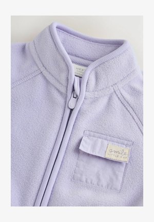 Giacca in pile lavanda con colletto alto, chiusura con zip e tasca sul petto con un'etichetta che recita "sorridi piccolo." Tessuto morbido.