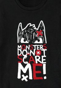 Schwarzes T-Shirt mit einem Grafikdesign eines Monstergesichts mit großen Augen, begleitet von dem Text "MONSTER MACHEN MIR KEINE ANGST!" in Rot und Weiß.