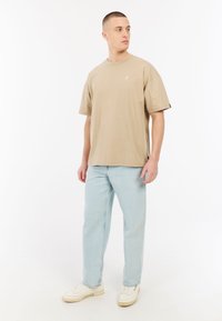 Beige katoenen t-shirt met verlaagde schouders, gecombineerd met lichtblauwe straight-leg jeans en witte sneakers. Minimalistisch ontwerp, geen patronen.