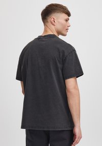 Tricou oversized din bumbac negru, cu guler rotund și mâneci scurte, cu cusături vizibile și un croi lejer. Vedere din spate prezentată.