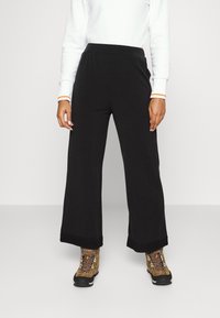 Svarta vida byxor med en mjuk textur, med ett bekvämt elastiskt midjeband. Kombinerat med bruna vandringskängor och en vit tröja.