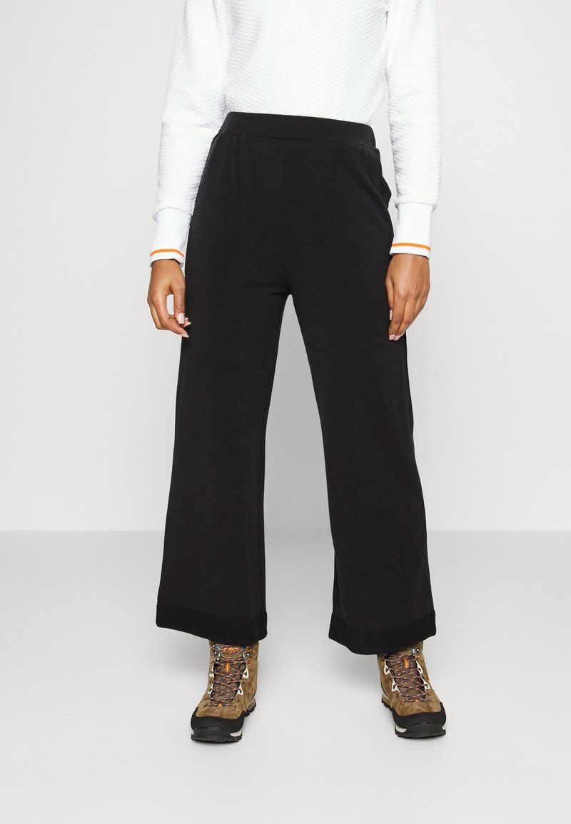 Svarta vida byxor med en mjuk textur, med ett bekvämt elastiskt midjeband. Kombinerat med bruna vandringskängor och en vit tröja.