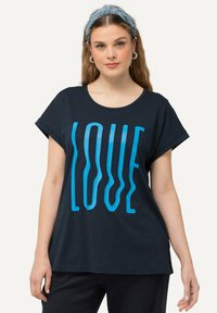 Camiseta de color azul marino hecha de algodón suave. Presenta un gráfico audaz y ondulado en azul claro que dice "AMOR". Mangas cortas enrolladas y un escote redondo.