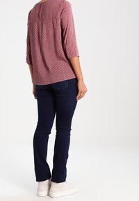 Blouse rose clair avec des points texturés, encolure ronde et panneau arrière uni. Associée à un jean slim bleu foncé et des baskets blanches.