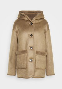 Tan hættejakke i shearling med fire sorte knapper foran og to store forlommer med blød fleecekant.
