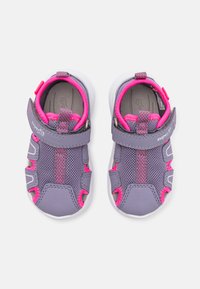 Lila Netzsneaker mit pinken Akzenten, grauem Innenfutter, verstellbarem Riemen und strapazierfähigen weißen Gummisohlen. Verfügt über Belüftungsöffnungen.