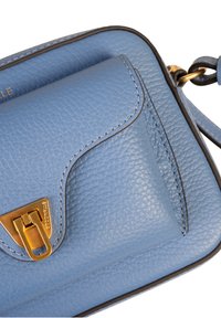 Jasnoniebieska skórzana torebka crossbody o teksturowanej powierzchni, z złotymi akcentami i kontrastowym przeszyciem. Posiada zapięcie na klapkę oraz regulowany pasek.