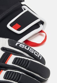 Black and white goalkeeper gloves with red accents, made from textured materials, featuring a Velcro strap and prominent brand logo.