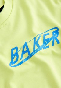 Tissu jaune vif avec le texte bleu "BAKER" et un texte plus petit "BY TED BAKER" imprimés en diagonale dessus.