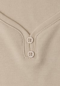 Tela de punto color beige con un escote en V profundo y dos botones de color claro en el centro. Textura suave con finos detalles de costura.