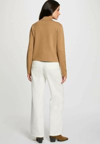 Maglione di maglia marrone con colletto corto, abbinato a jeans bianchi a gamba larga e stivali alla caviglia marroni con tacco. Design semplice, senza motivi.