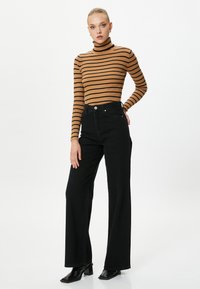 Braun und schwarz gestreifter Rollkragenpullover kombiniert mit hochtaillierten, schwarzen Weitbeinjeans und schwarzen Blockabsatzschuhen.