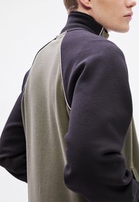 Polár pulóver sötétzöld hátrésszel és fekete ujjal. Magas gallérral és fehér paszpóllal a vállvarrások mentén.