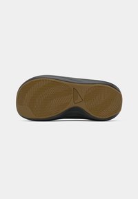 Czarna podeszwa sneakerów z teksturowanym wzorem gumowym, z tanowym gripem w kształcie rybiej ości na środku i gładkimi krawędziami.