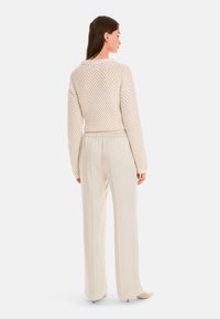 Knit cardigan in off-white with a textured pattern, paired with light beige, wide-leg trousers. Both pieces feature a relaxed fit.