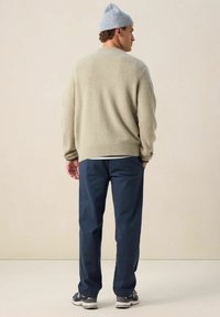 Pull léger vert avec des poignets et un ourlet côtelés, assorti à un pantalon bleu marine et un bonnet en tricot bleu clair. Tenue décontractée vue de dos.
