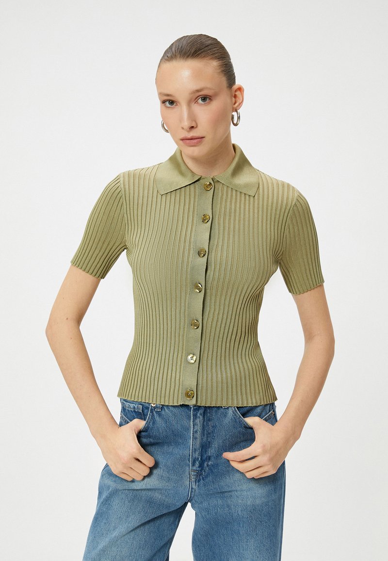 Top a maniche corte a righe di colore verde chiaro con colletto, caratterizzato da sette bottoni dorati sul davanti e una vestibilità aderente.