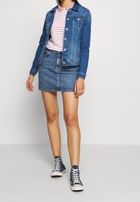 Chaqueta de denim con mangas largas y bolsillos frontales, combinada con una camiseta tipo polo a rayas rosa y blanca y una falda de denim, complementada con zapatillas altas azules.
