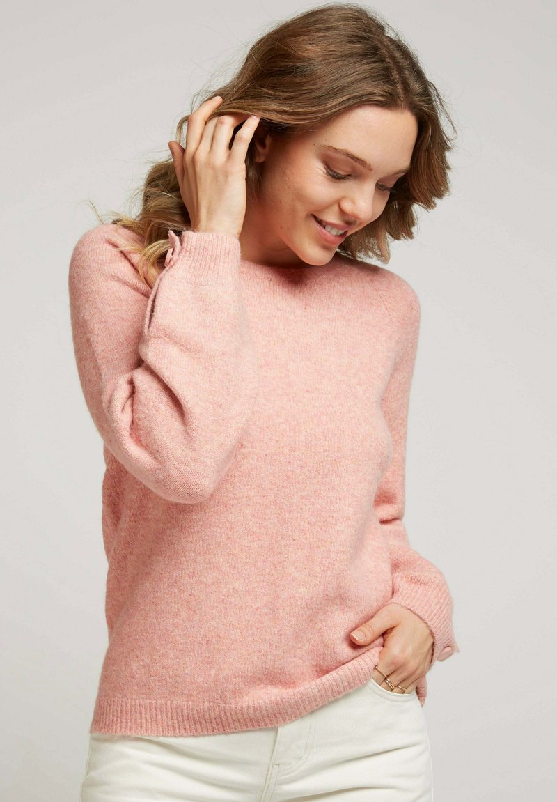 Pull léger rose fabriqué à partir d'un matériau doux et texturé. Il présente un col rond et des poignets côtelés, avec une coupe décontractée et peu de détails.