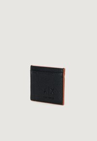 Tarjetero de cuero texturizado negro con bordes marrones, estampado con el logotipo "A|X Armani Exchange" en la parte frontal, mostrado sobre un fondo liso.