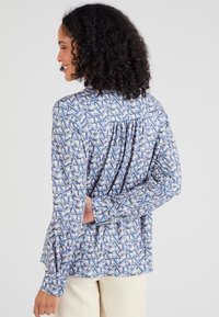 Camicia con bottoni caratterizzata da un motivo geometrico blu, bianco e rosa; presenta maniche lunghe, schiena plissettata e colletto classico.