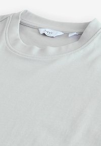 Lys grå T-shirt med ribbet rund halsudskæring, lavet af struktureret stof. Har en afslappet pasform og en synlig labelmærke indeni kraven.