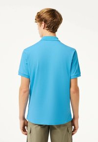 Vaaleansininen lyhythihainen polo-paita, jossa on käännetty kaulus. Sileä rakenne ja suora helma, yhdistettynä vaaleisiin cargo-housuihin.