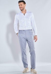 Hellgraue, taillierte Hose mit einem dezenten strukturierten Muster, kombiniert mit einem weißen Hemd und beigen Slip-on-Schuhen.