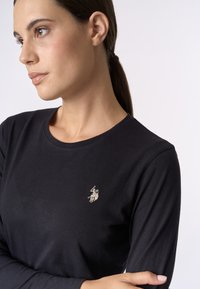 Maglietta nera a maniche lunghe realizzata in un tessuto morbido, con un piccolo e intricato logo ricamato sul petto. Design semplice e aderente.
