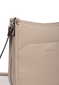 Borsa a tracolla in pelle beige con superficie texturizzata, parte superiore curvata, cuciture decorative e un dettaglio con logo. Tracolla regolabile.