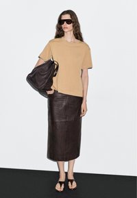 Beige übergroßes T-Shirt, brauner Leder-Midirock, dunkle Sonnenbrille, braune Tote-Bag und braune Sandalen. Geschmeidige Texturen, minimalistisches Design.