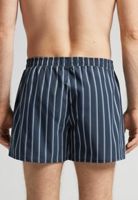 Námořnické modré plavky s pruhy vyrobené z lehkého, hladkého materiálu s elastickým pasem a uvolněným střihem, se bílými vertikálními pruhy.